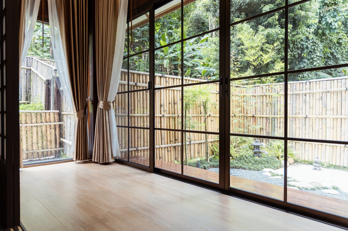A spacious room with large glass sliding door overlooking bamboo fence and garden with greenery and stone lantern peaceful natural light wooden floor